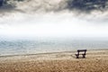 Empty wooden bench on the beach in cloudy weather Royalty Free Stock Photo