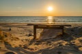 Empty wooden bench and beautiful golden sunset at the beach. Sun setting into the sea on tranquil evening. Nobody Royalty Free Stock Photo