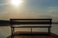 Empty wooden bench on the pier by the river under the rays of the setting sun in the evening fog Royalty Free Stock Photo