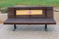 Empty wooden bench in the public park in Abu Dhabi with sign `For your safety keep distance`
