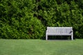 An empty wooden bench on the right of a green field with a background of green big bush and space on the left to be filled in.