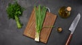 Empty wooden board, green onions, bunch of dill and parsley on a black table, top view Royalty Free Stock Photo