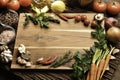 Empty wooden cutting board with copy space surrounded by peppers, herbs, tomatoes, mushrooms and other delicious flavoured vegetab Royalty Free Stock Photo