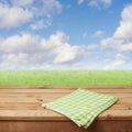 Empty wooden deck table with checked tablecloth over green grass meadow and blue sky background for product montage Royalty Free Stock Photo
