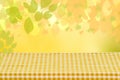 Empty wooden desk table with yellow checkered tablecloth over abstract bright light green yellow spring or summer background. Royalty Free Stock Photo