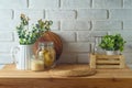 Empty wooden kitchen table with wicker place mat, food jars and plants over white brick wall background. Kitchen mock up for Royalty Free Stock Photo