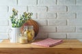 Empty wooden l table with tablecloth, plant, food jars and cutting board over white brick wall background. Kitchen mock up for Royalty Free Stock Photo