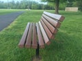 Empty wooden park bench surrounded by green grass and trees