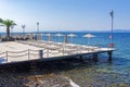 Empty wooden sunbathing deck with chairs and umbrellas by a calm blue sea under the bright sun in summer