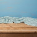 Empty wooden table with checked blue tablecloth over rustic painted wall