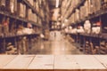 Empty wooden table on defocuced blurred boxes on rows of shelves