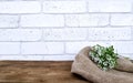 Empty wooden table with flowers and burlap fabric on white bricks wall background.