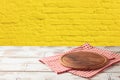 Empty wooden table with pizza board and tablecloth over yellow brick stone wall background