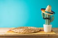 Empty wooden table with wicker place mat and cactus decoration over blue wall background. Mexican party mock up for design and