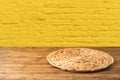 Empty wooden table with wicker round placemat over yellow brick wall background