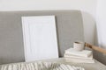 Empty wooden vertical picture frame mockup. Cup of coffee on pile of old books. Midcentury linen sofa. White wall Royalty Free Stock Photo