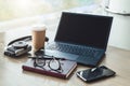 Empty workplace. Near window on desk is laptop, smartphone, notebook, glasses, cup of coffee, camera for instant photos. Royalty Free Stock Photo