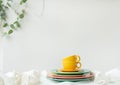 Empty yellow cups and brightly colored plates on a white table covered with a linen tablecloth, a flower pot on the wall Royalty Free Stock Photo