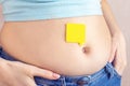 An empty yellow paper blank message on belly fat with hands squeezes at the waist of a young woman in jeans. The concept of excess Royalty Free Stock Photo