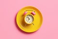 Empty yellow plate with alarm clock on pink background, intermittent fasting concept. Royalty Free Stock Photo