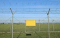 Empty yellow sign outside a double wire mesh barrier with barbed wire on top.