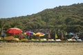 Empty yellow sun loungers under multi-colored beach umbrellas on the yellow sand against the background of a green mountain with Royalty Free Stock Photo