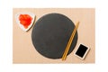 Emptyround black slate plate with chopsticks for sushi, ginger and soy sauce on brown sushi mat background. Top view with copy Royalty Free Stock Photo