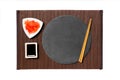 Emptyround black slate plate with chopsticks for sushi, ginger and soy sauce on dark bamboo mat background. Top view with copy Royalty Free Stock Photo