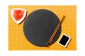 Emptyround black slate plate with chopsticks for sushi, ginger and soy sauce on yellow bamboo mat background. Top view with copy Royalty Free Stock Photo