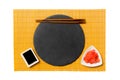 Emptyround black slate plate with chopsticks for sushi, ginger and soy sauce on yellow bamboo mat background. Top view with copy Royalty Free Stock Photo