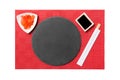 Emptyround black slate plate with chopsticks for sushi and soy sauce, ginger on red mat sushi background. Top view with copy space Royalty Free Stock Photo