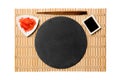Emptyround black slate plate with chopsticks for sushi and soy sauce, ginger on yellow bamboo mat background. Top view with copy Royalty Free Stock Photo