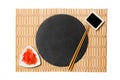 Emptyround black slate plate with chopsticks for sushi and soy sauce, ginger on yellow bamboo mat background. Top view with copy Royalty Free Stock Photo