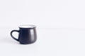 Enamel black mug on white table background mockup. Boho style classic stock photo. Still life composition with black ceramic cup.