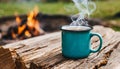 Enamel cup of hot steaming coffee on old log by an outdoor campfire. Tasty drink Royalty Free Stock Photo