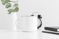 Enamel mug mockup with eucalyptus in a vase and workspace accessories on a white table