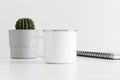 Enamel mug mockup with a notebook and a cactus in a pot on white table