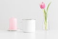 Enamel mug mockup with pink tulips in a vase and candle on a white table Royalty Free Stock Photo