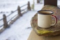 Enamel mug on the stone on a wooden veranda in winter on a rustic background.