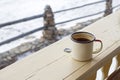 Enamel mug with strong tea and tea bag on a wooden fence on a snowy winter background.