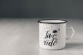 Enamel white metal mug with black line on the edge with the inscription on white wooden table on gray background. Place for text