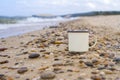 Enameled camp mug on the pebbles of the sandy shore of Lake Baikal during a wave on a mountain background in the summer.
