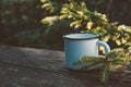 Enameled cup of coffee or tea on wooden board in summer forest