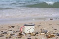Enameled metal hiking tourist mug on the rocks and sand of the picturesque Lake Baikal in summer on a background of waves.