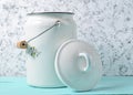 Enameled milk can with lid on white concrete wall background.
