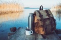 Mug of coffee or tea, backpack of traveller and thermos on wooden pier on tranquil lake