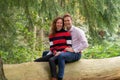 Enamored couple sits on a thick tree trunk, the man sits behind the woman. In side view