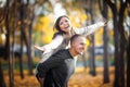 Enamoured young couple fool around in autumn outdoor. A man rolls a woman on his back, and she depicts a flight Royalty Free Stock Photo