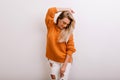 Enchanting female model in trendy ripped pants looking down while posing in studio. Indoor portrait of graceful blonde