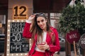 Enchanting lady in red jacket posing with tongue out on the street. Charming woman with long brown hair standing near